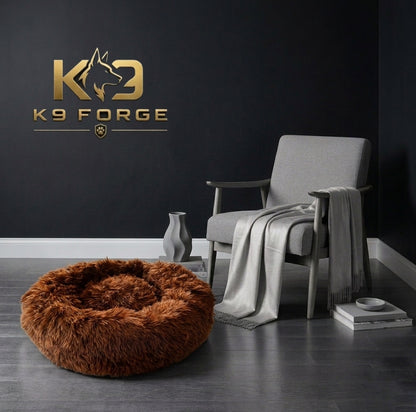 Brown fluffy dog bed in a room with a gray chair and K9 Forge logo on the wall.